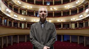 In questa foto, un uomo è in posa in piedi, dietro di lui si vede la platea di un grande teatro. L'uomo è Mauro Pescio, autore e attore dello spettacolo Io ero il Milanese.